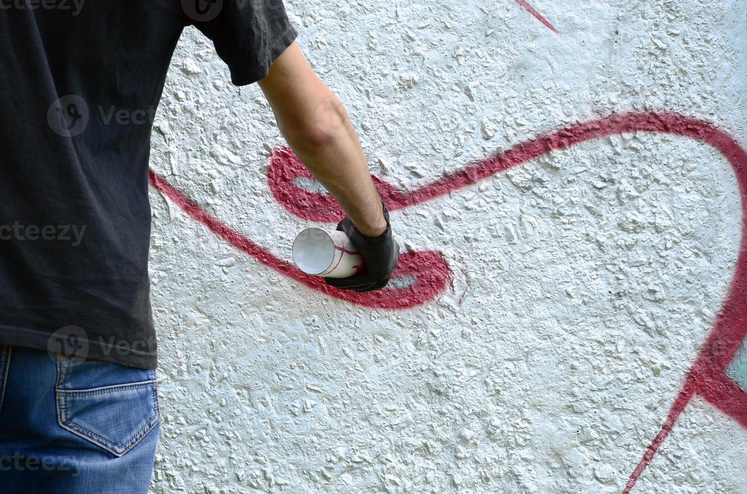 A young hooligan paints graffiti on a concrete wall. Illegal vandalism concept. Street art photo