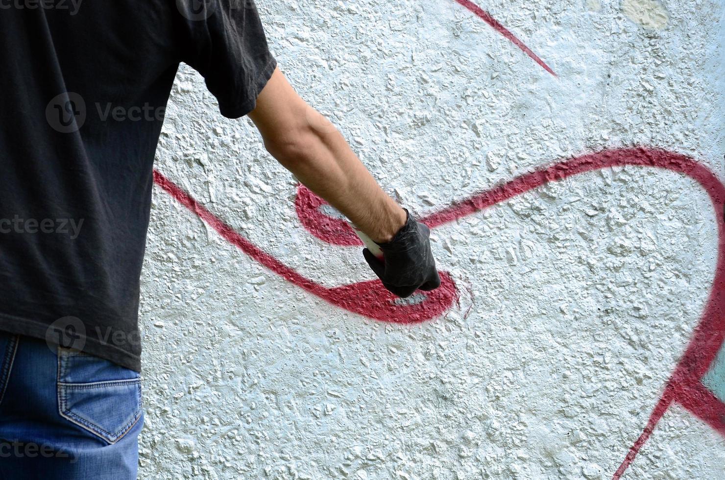 A young hooligan paints graffiti on a concrete wall. Illegal vandalism concept. Street art photo