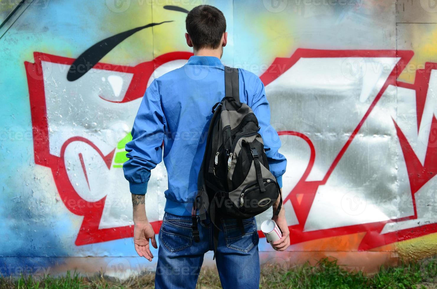 A young graffiti artist with a black bag looks at the wall with his graffiti on a wall. Street art concept photo