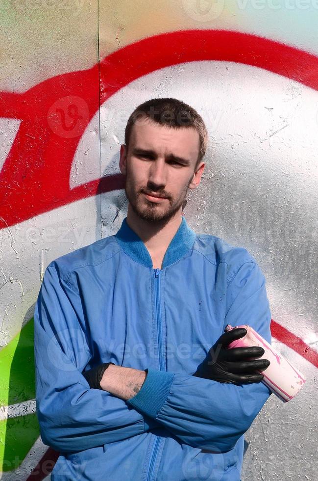 The graffiti artist with spray can poses against the background of a colorful painted wall. Street art concept photo