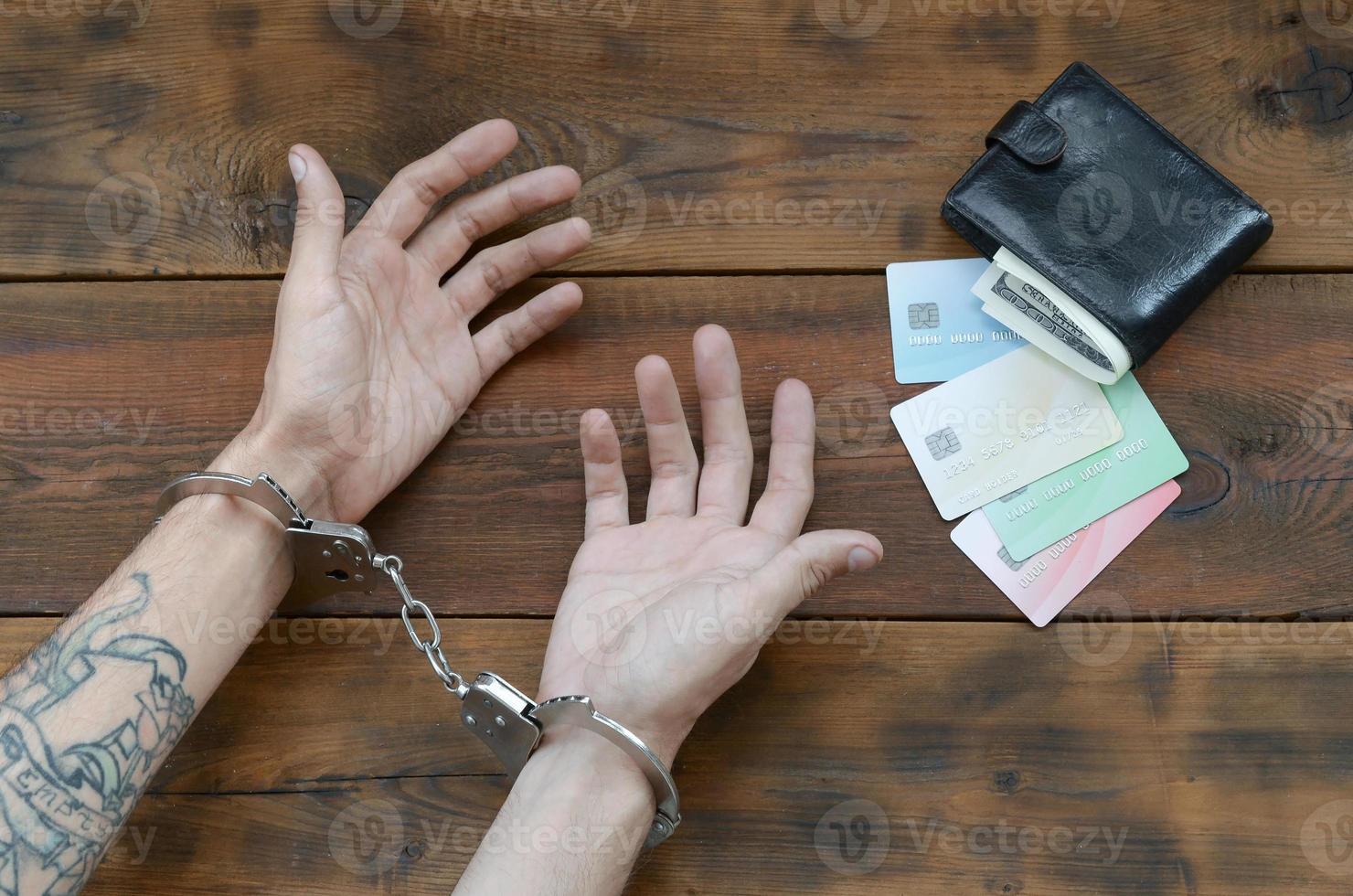 Cuffed hands of tattooed criminal suspect of carding and fake credit cards with cash in purse as evidence for investigation photo