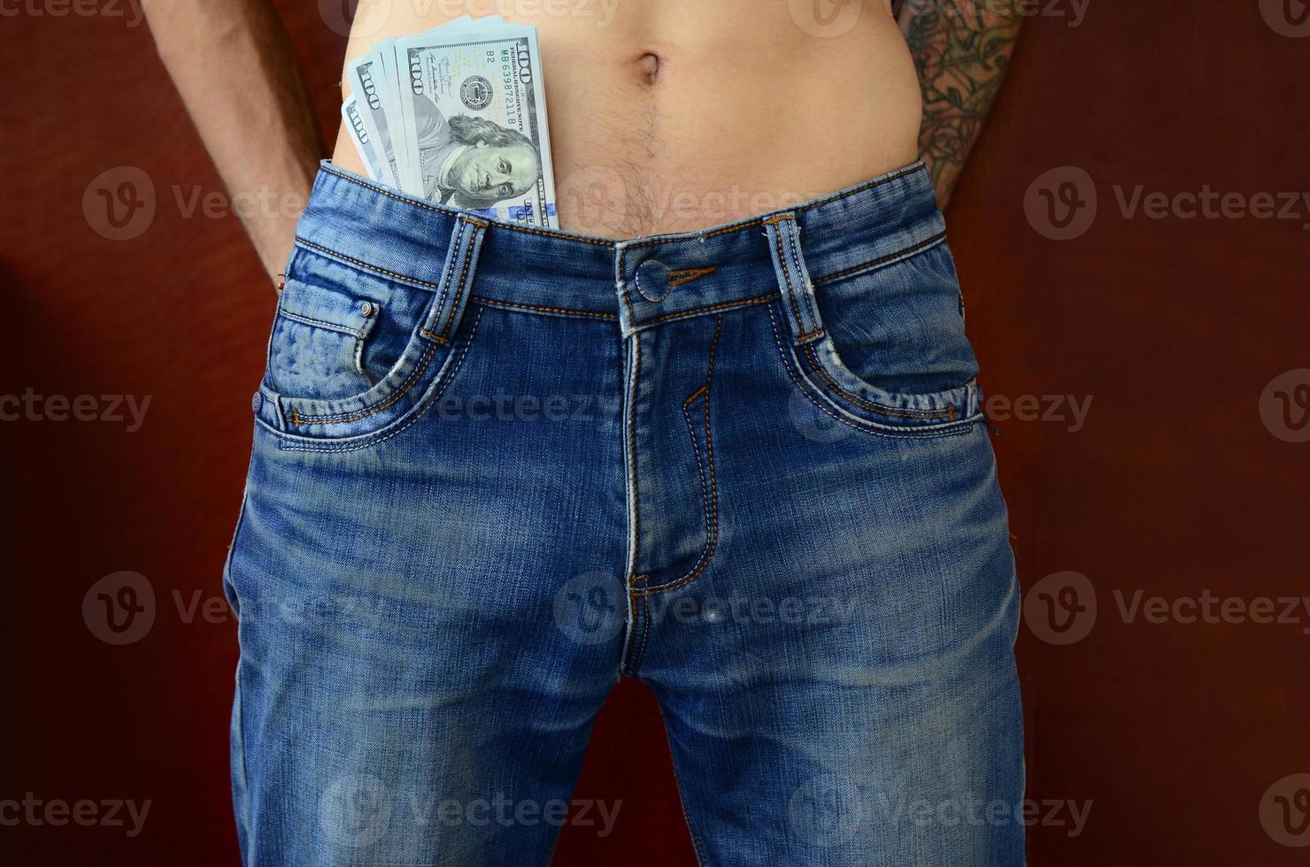 The body of a guy in blue jeans with a lot of dollar bills, visible from under the clothes photo