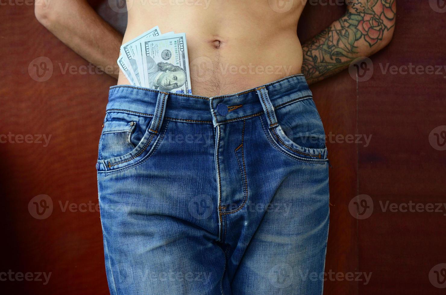 The body of a guy in blue jeans with a lot of dollar bills, visible from under the clothes photo