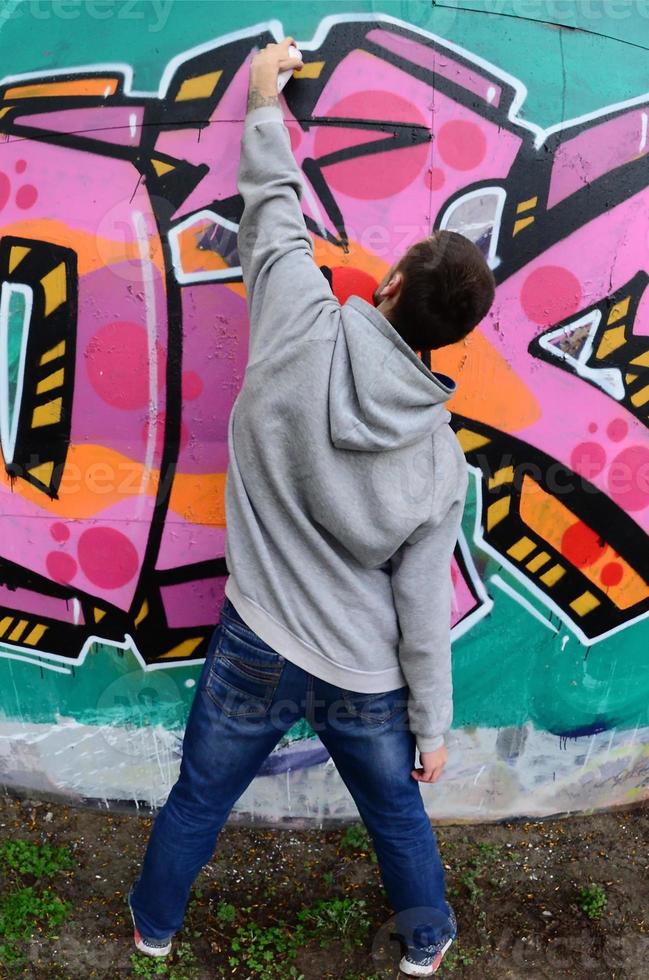 un joven con una sudadera con capucha gris pinta graffiti en rosa y verde c foto