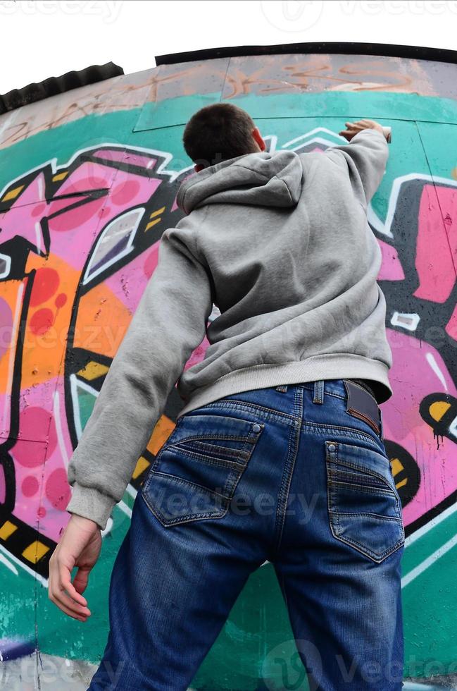 A young guy in a gray hoodie paints graffiti in pink and green c photo