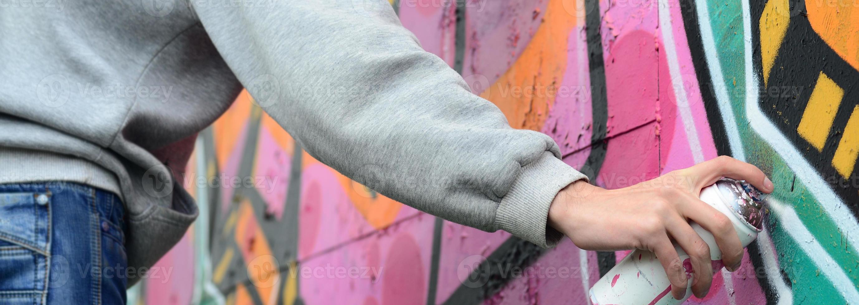 A young guy in a gray hoodie paints graffiti in pink and green c photo