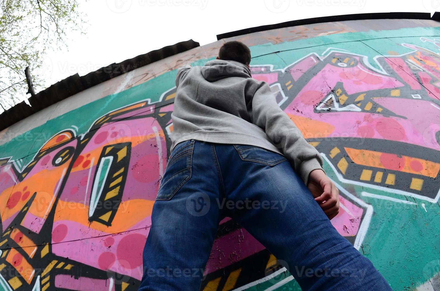 A young guy in a gray hoodie paints graffiti in pink and green c photo