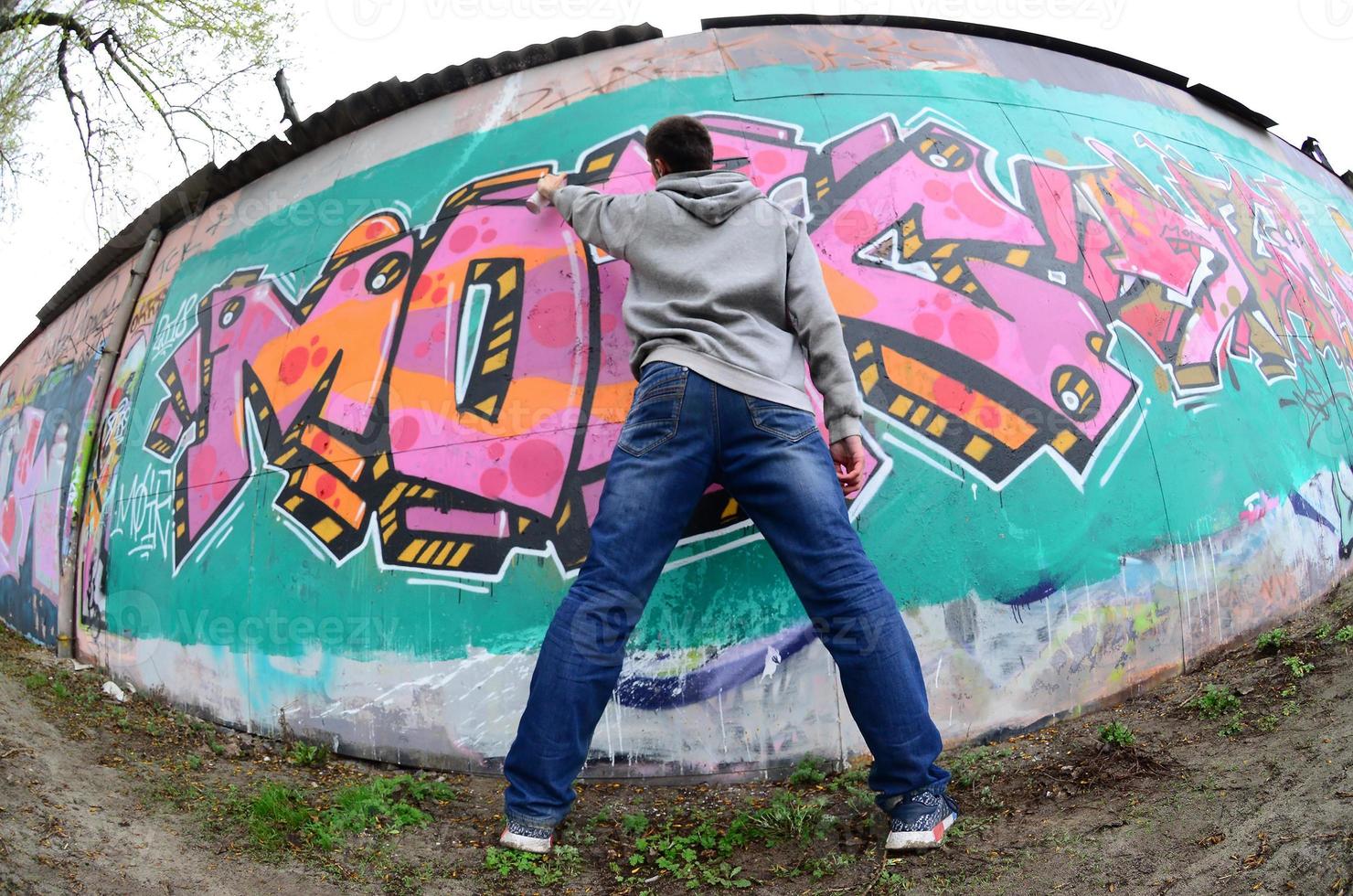 un joven con una sudadera con capucha gris pinta graffiti en rosa y verde c foto