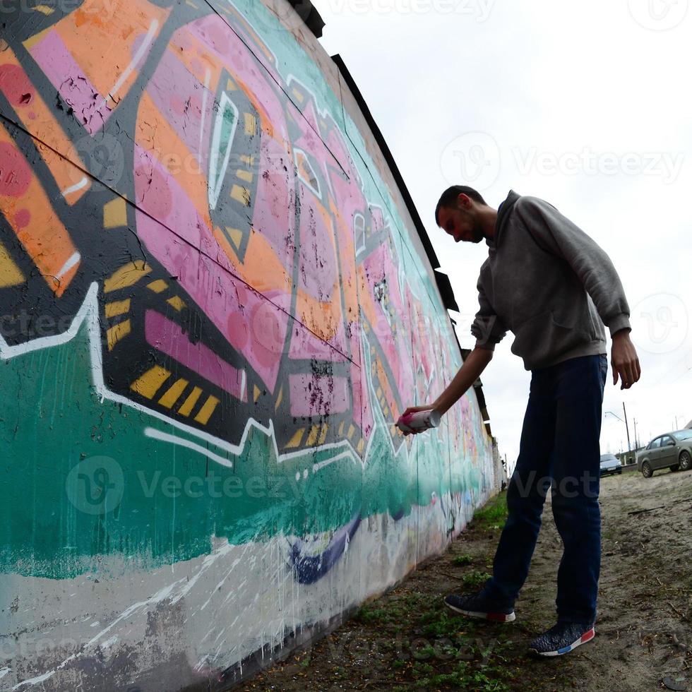 A young guy in a gray hoodie paints graffiti in pink and green c photo