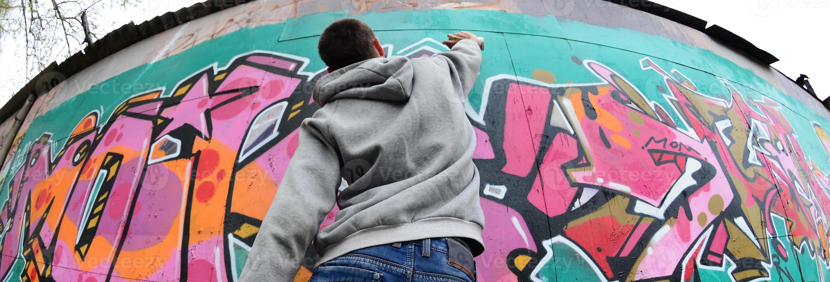 A young guy in a gray hoodie paints graffiti in pink and green c photo