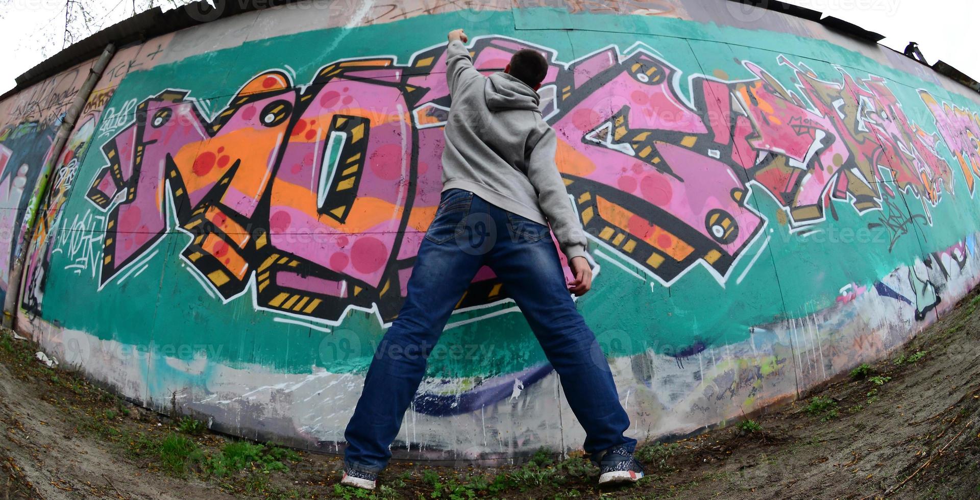 A young guy in a gray hoodie paints graffiti in pink and green c photo