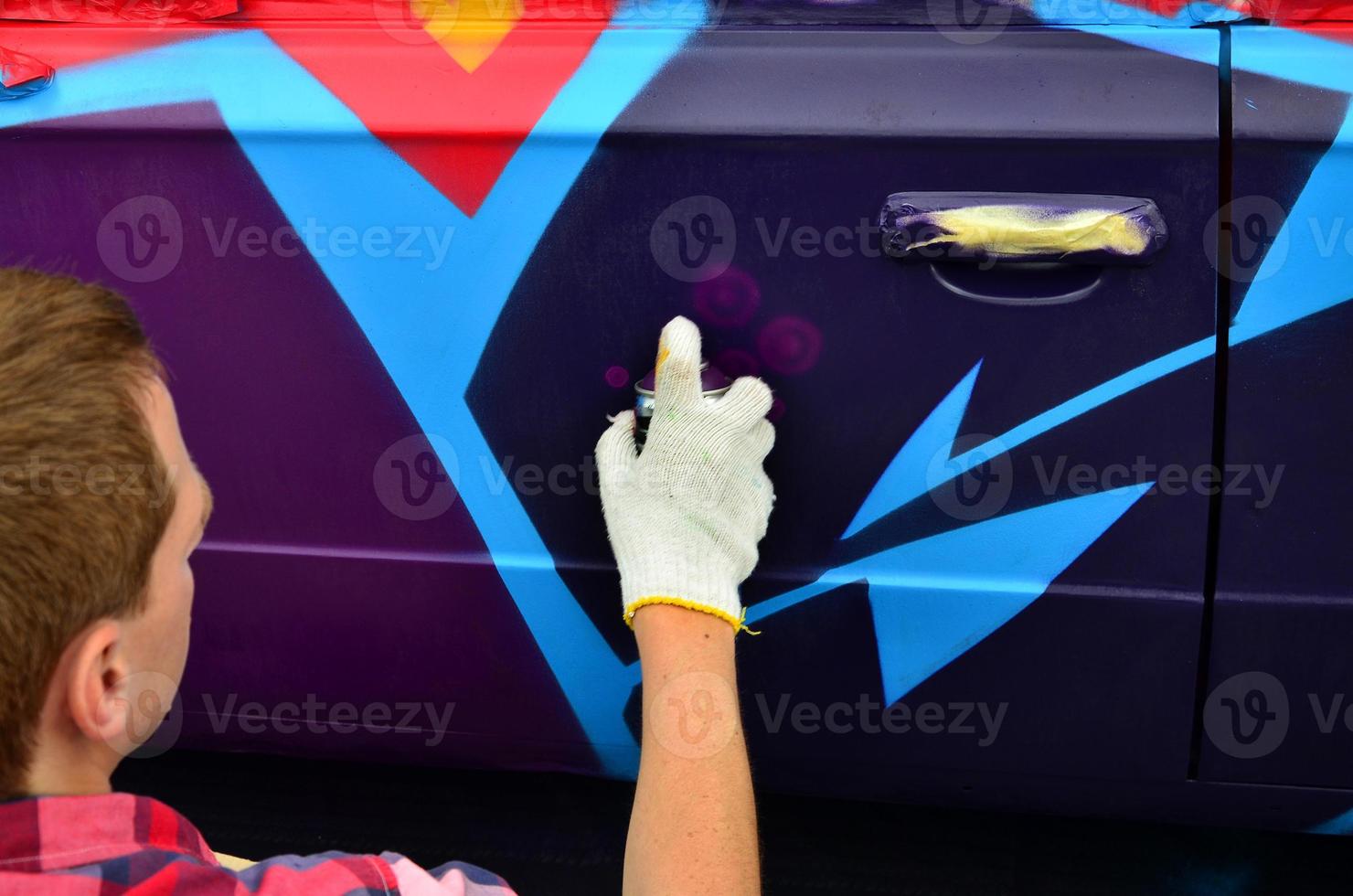 un joven grafitero pelirrojo pinta un nuevo grafiti colorido en el camión. foto del proceso de dibujo de un grafiti en el primer plano de un coche. el concepto de arte callejero y vandalismo ilegal
