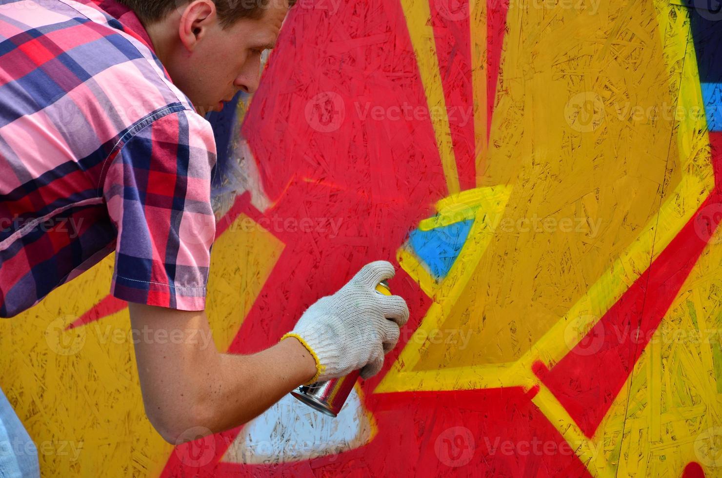 A young red-haired graffiti artist paints a new graffiti on the wall. Photo of the process of drawing a graffiti on a wall close-up. The concept of street art and illegal vandalism
