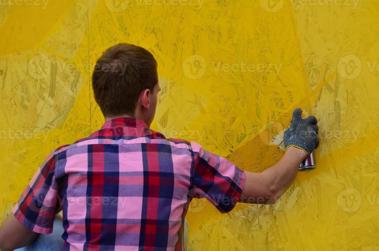 A young red-haired graffiti artist paints a new graffiti on the wall. Photo of the process of drawing a graffiti on a wall close-up. The concept of street art and illegal vandalism