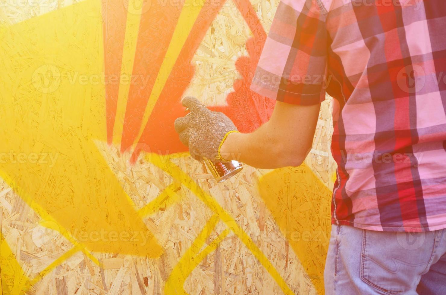 A hand with a spray can that draws a new graffiti on the wall. Photo of the process of drawing a graffiti on a wooden wall close-up. The concept of street art and illegal vandalism
