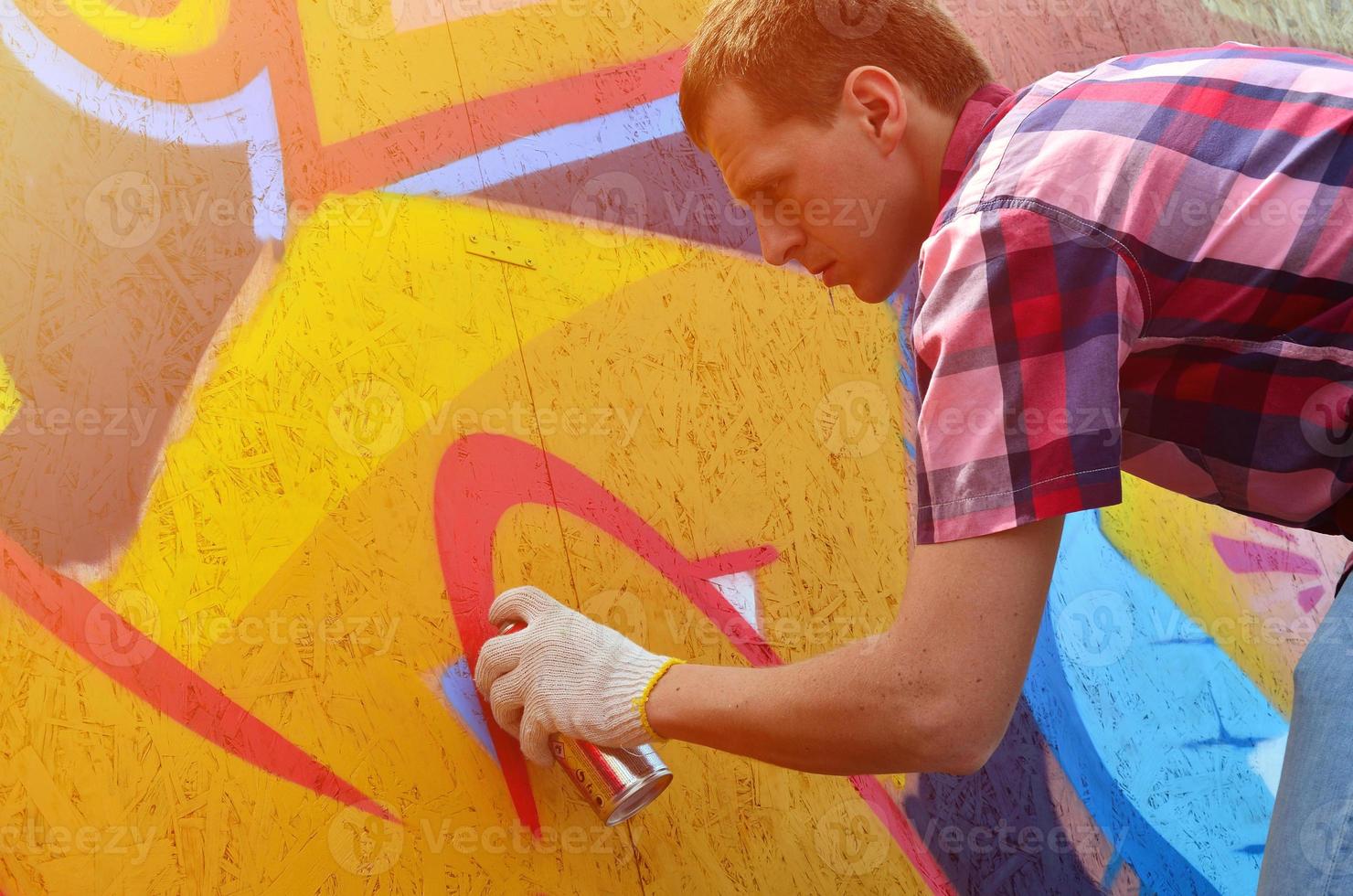 A young red-haired graffiti artist paints a new graffiti on the wall. Photo of the process of drawing a graffiti on a wall close-up. The concept of street art and illegal vandalism