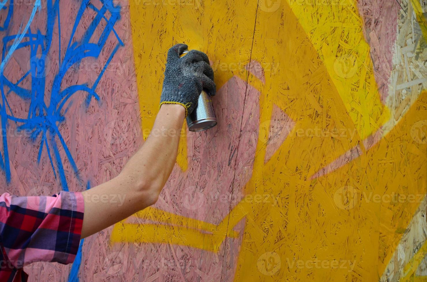 A hand with a spray can that draws a new graffiti on the wall. Photo of the process of drawing a graffiti on a wooden wall close-up. The concept of street art and illegal vandalism