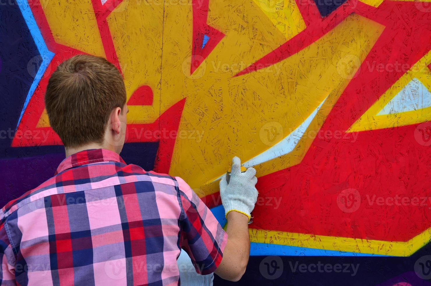 A young red-haired graffiti artist paints a new graffiti on the wall. Photo of the process of drawing a graffiti on a wall close-up. The concept of street art and illegal vandalism