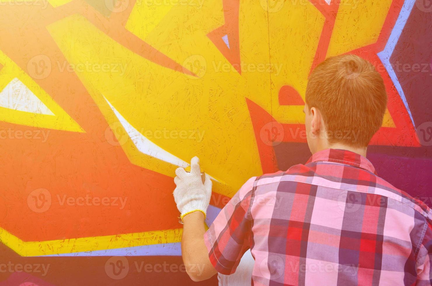 A young red-haired graffiti artist paints a new graffiti on the wall. Photo of the process of drawing a graffiti on a wall close-up. The concept of street art and illegal vandalism