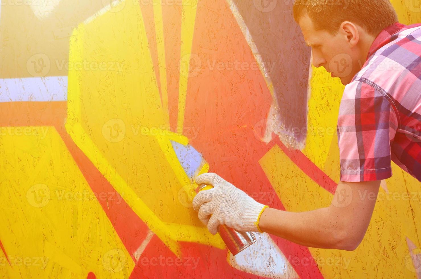 A young red-haired graffiti artist paints a new graffiti on the wall. Photo of the process of drawing a graffiti on a wall close-up. The concept of street art and illegal vandalism