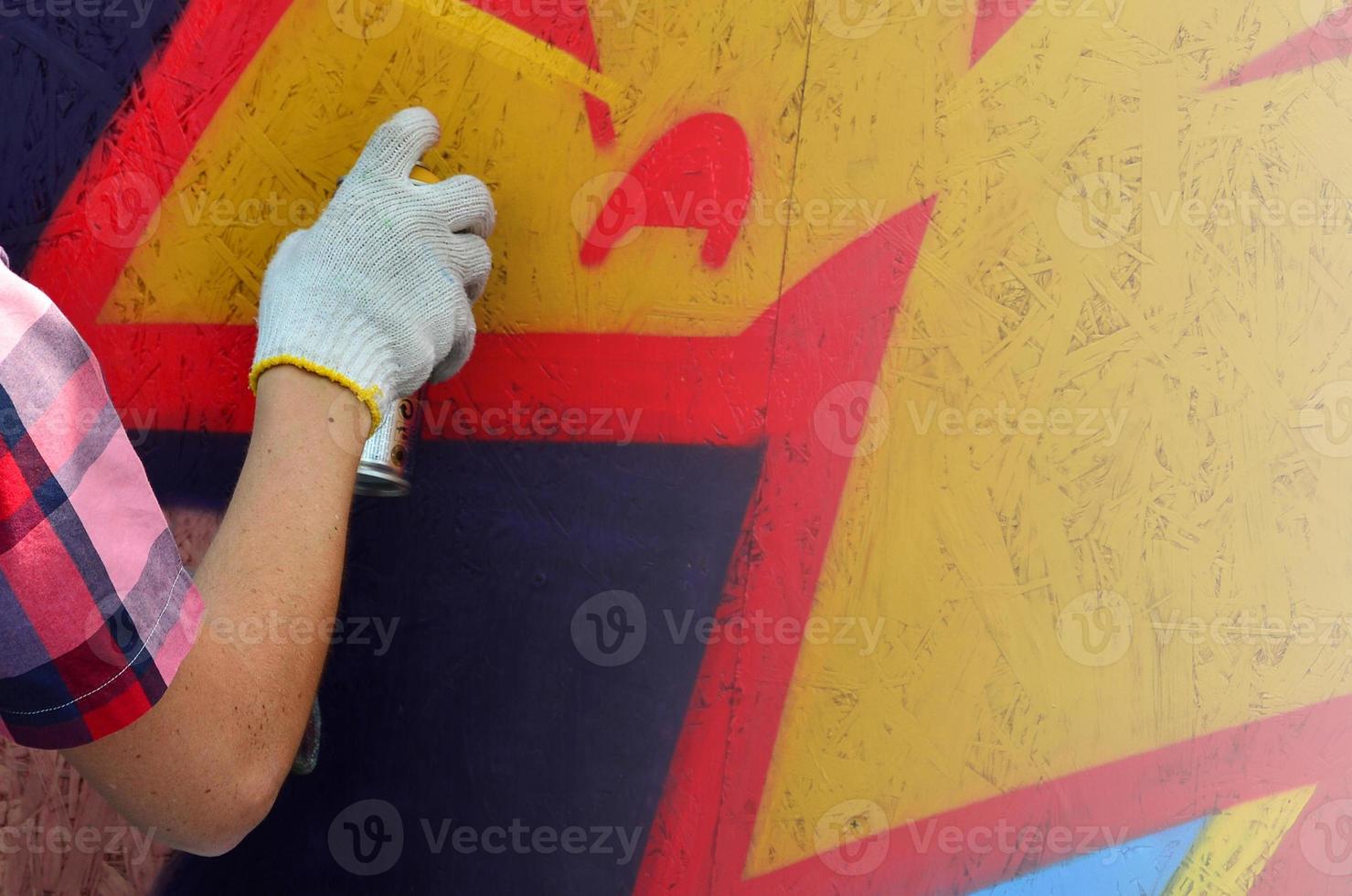 A hand with a spray can that draws a new graffiti on the wall. Photo of the process of drawing a graffiti on a wooden wall close-up. The concept of street art and illegal vandalism