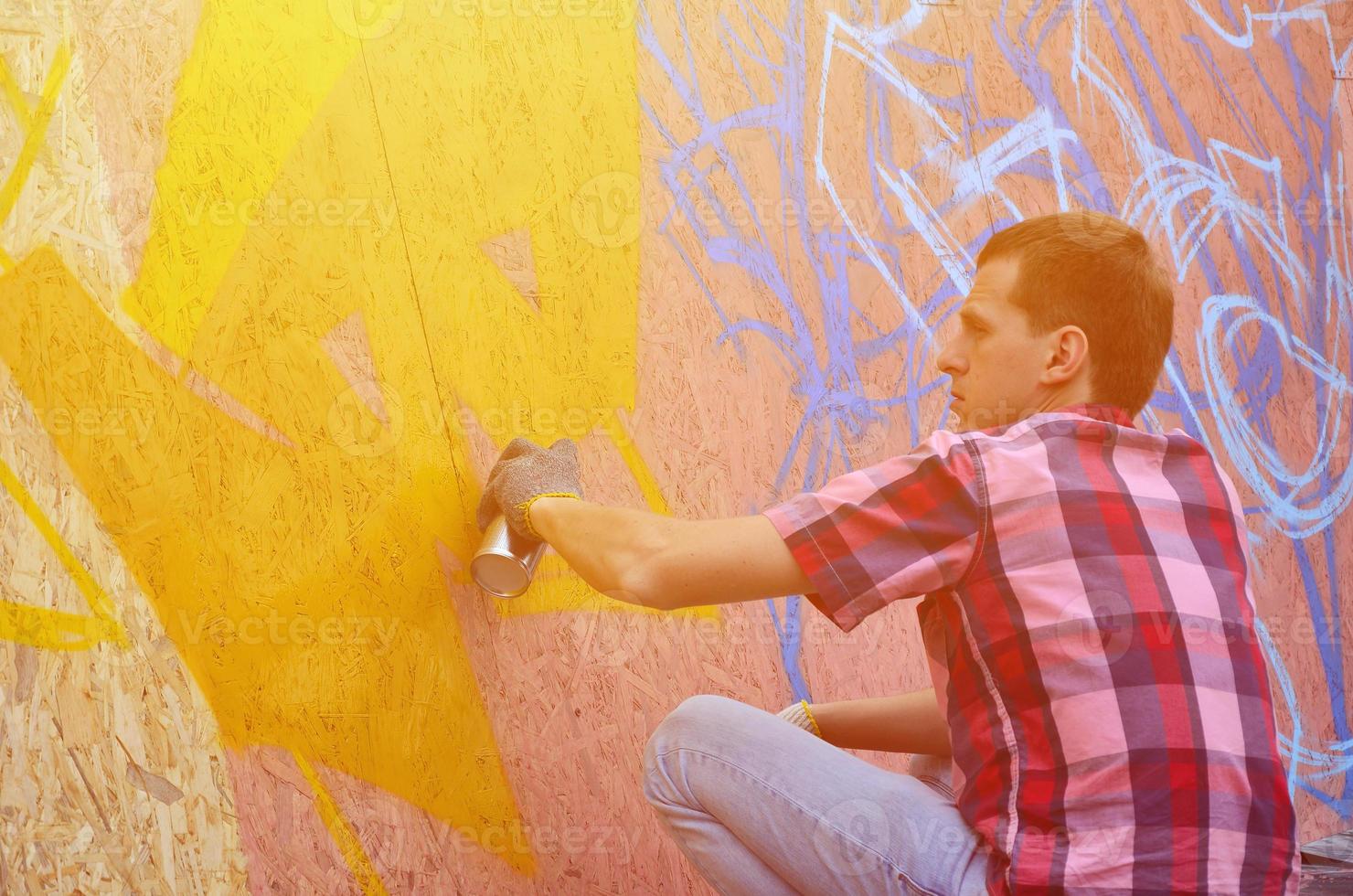 A young red-haired graffiti artist paints a new graffiti on the wall. Photo of the process of drawing a graffiti on a wall close-up. The concept of street art and illegal vandalism