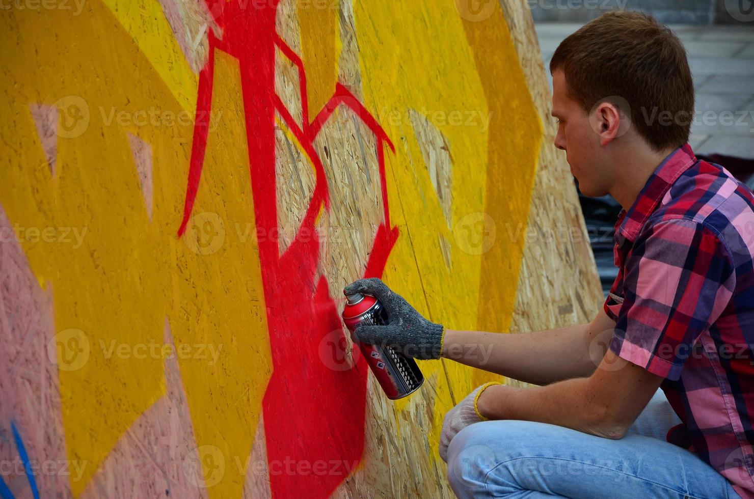 A young red-haired graffiti artist paints a new graffiti on the wall. Photo of the process of drawing a graffiti on a wall close-up. The concept of street art and illegal vandalism