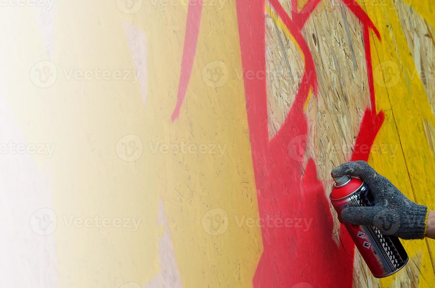 A hand with a spray can that draws a new graffiti on the wall. Photo of the process of drawing a graffiti on a wooden wall close-up. The concept of street art and illegal vandalism