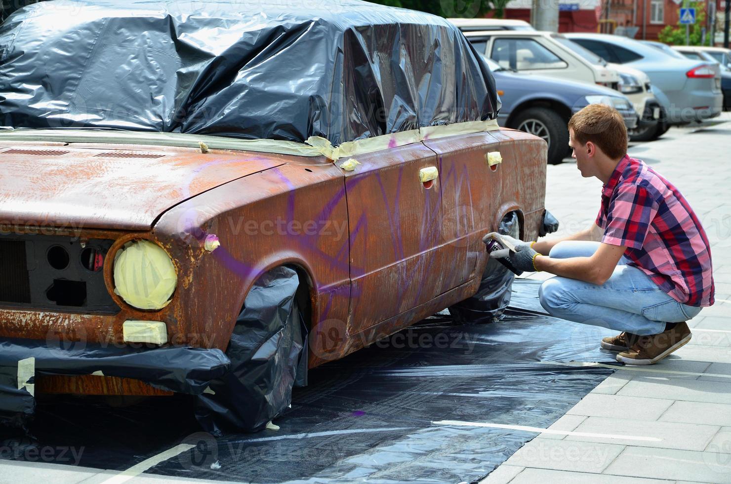 un joven grafitero pelirrojo pinta un nuevo grafiti colorido en el camión. foto del proceso de dibujo de un grafiti en el primer plano de un coche. el concepto de arte callejero y vandalismo ilegal