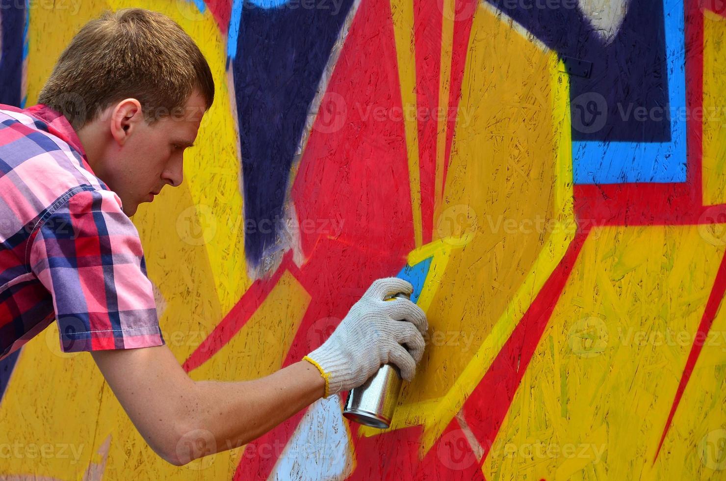 A young red-haired graffiti artist paints a new graffiti on the wall. Photo of the process of drawing a graffiti on a wall close-up. The concept of street art and illegal vandalism
