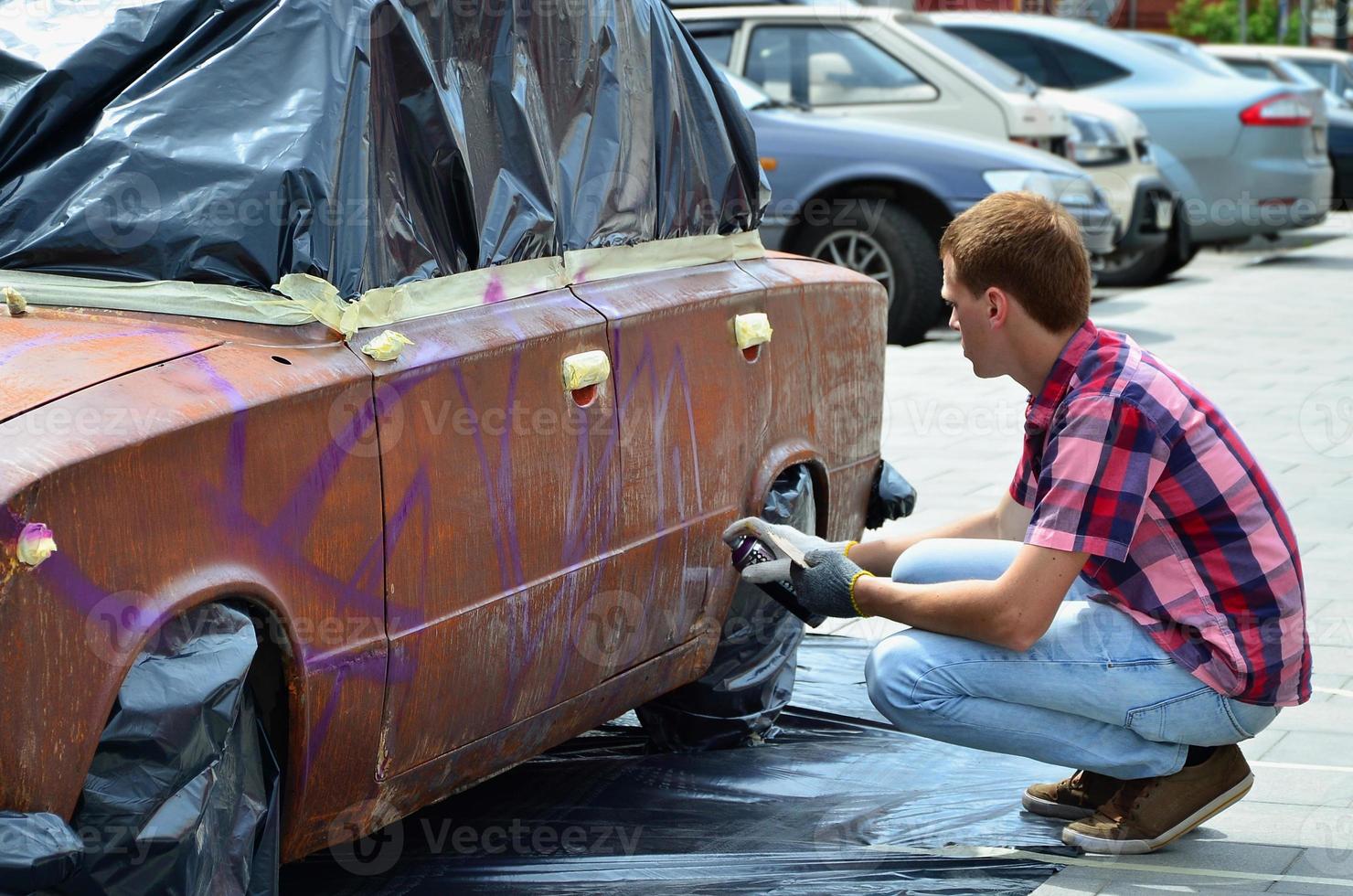 un joven grafitero pelirrojo pinta un nuevo grafiti colorido en el camión. foto del proceso de dibujo de un grafiti en el primer plano de un coche. el concepto de arte callejero y vandalismo ilegal