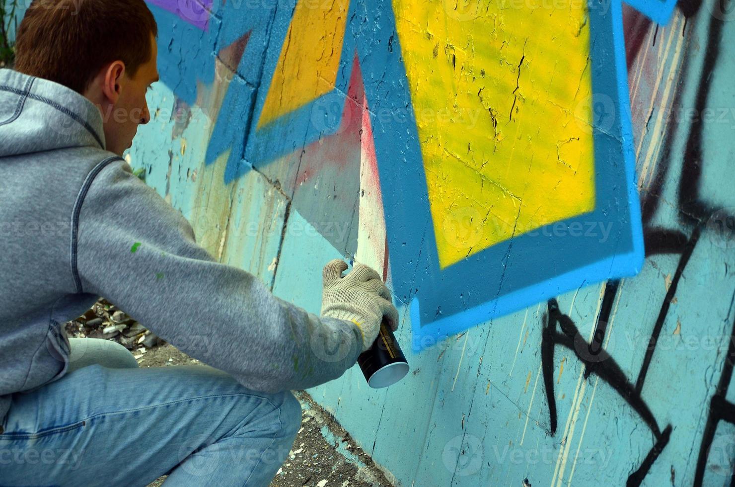 A young red-haired graffiti artist paints a new graffiti on the wall. Photo of the process of drawing a graffiti on a wall close-up. The concept of street art and illegal vandalism