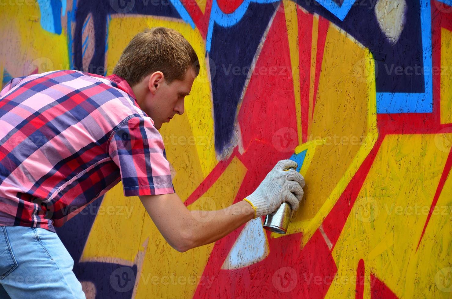 A young red-haired graffiti artist paints a new graffiti on the wall. Photo of the process of drawing a graffiti on a wall close-up. The concept of street art and illegal vandalism