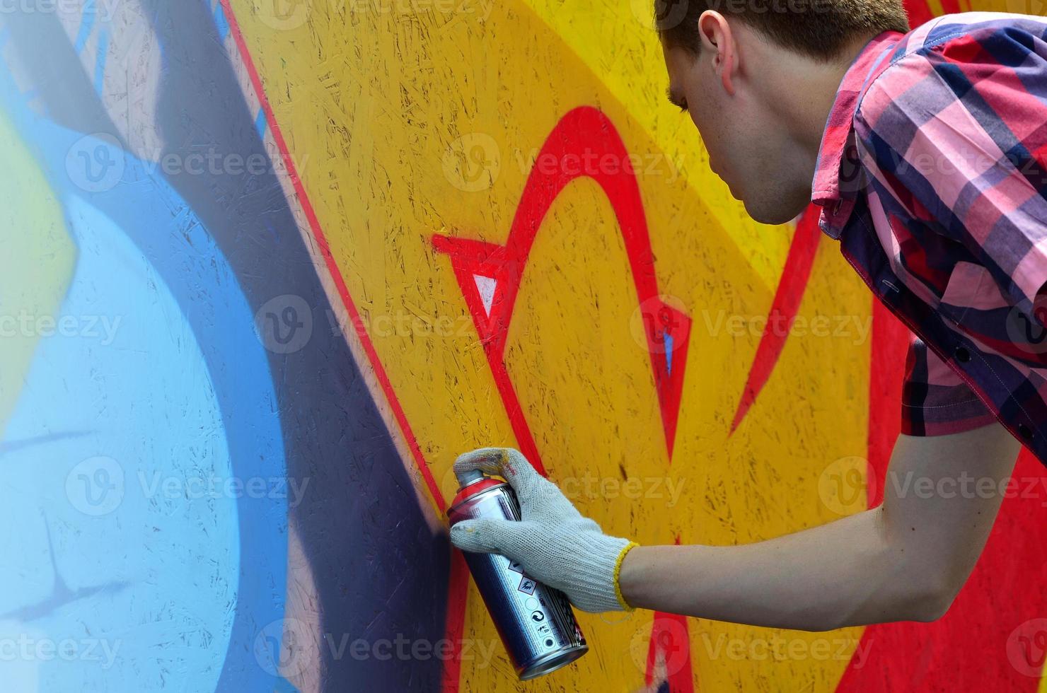 A young red-haired graffiti artist paints a new graffiti on the wall. Photo of the process of drawing a graffiti on a wall close-up. The concept of street art and illegal vandalism