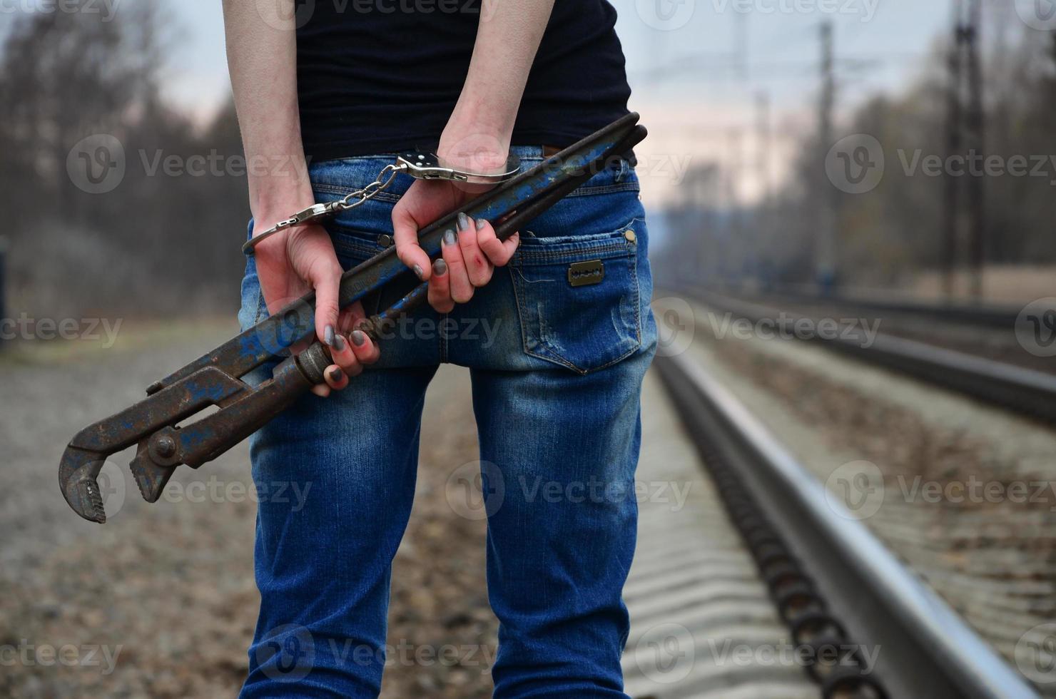 The girl in handcuffs with the pipe wrench on the railway track photo
