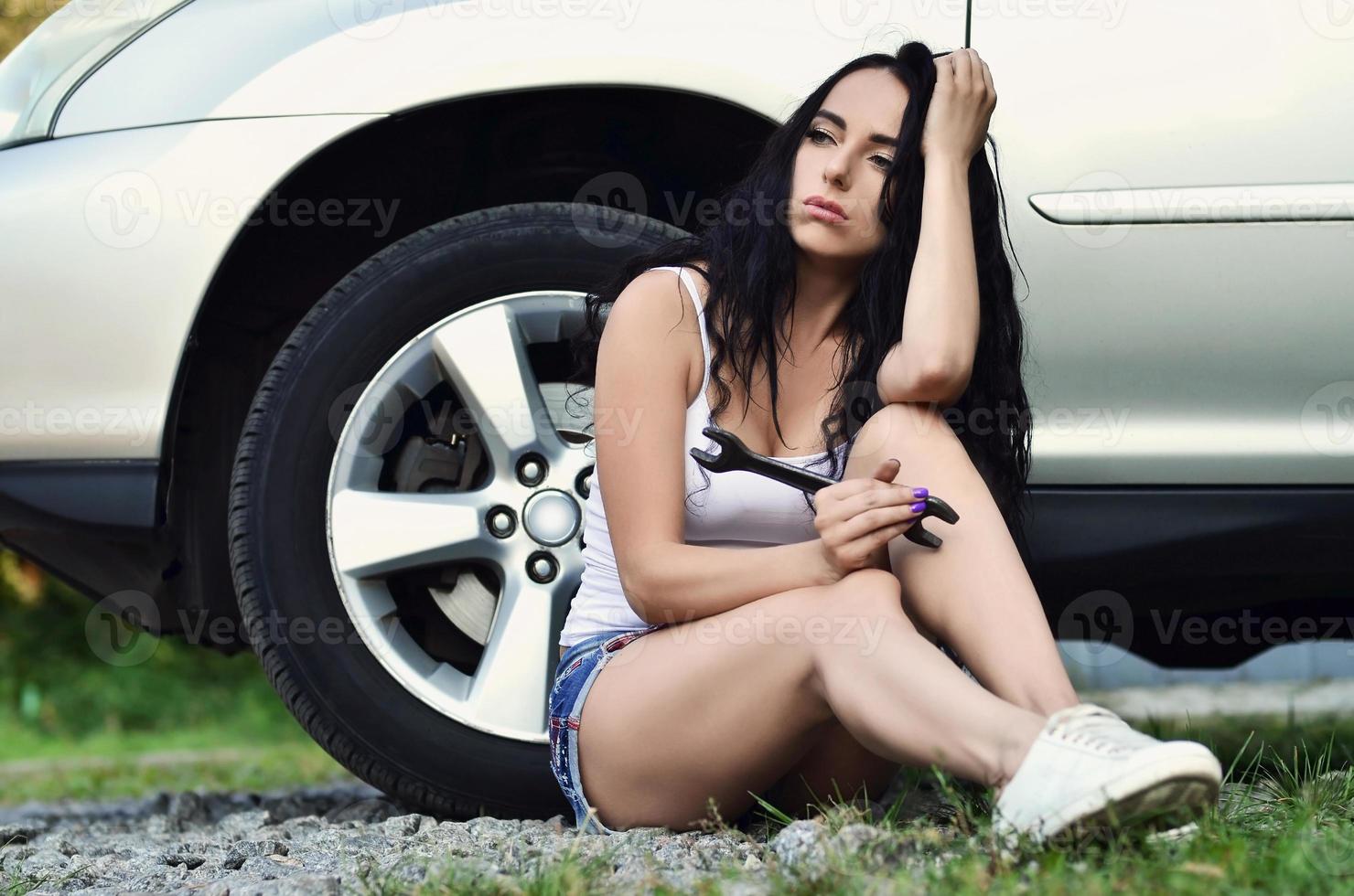 chica joven y sexy con llave inglesa cerca de un auto plateado con una o foto