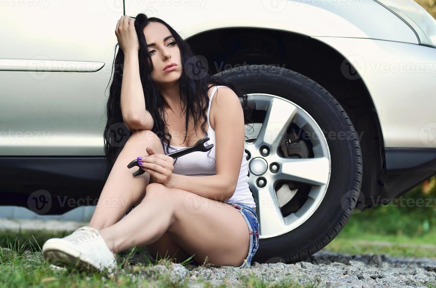 chica joven y sexy con llave inglesa cerca de un auto plateado con una o foto