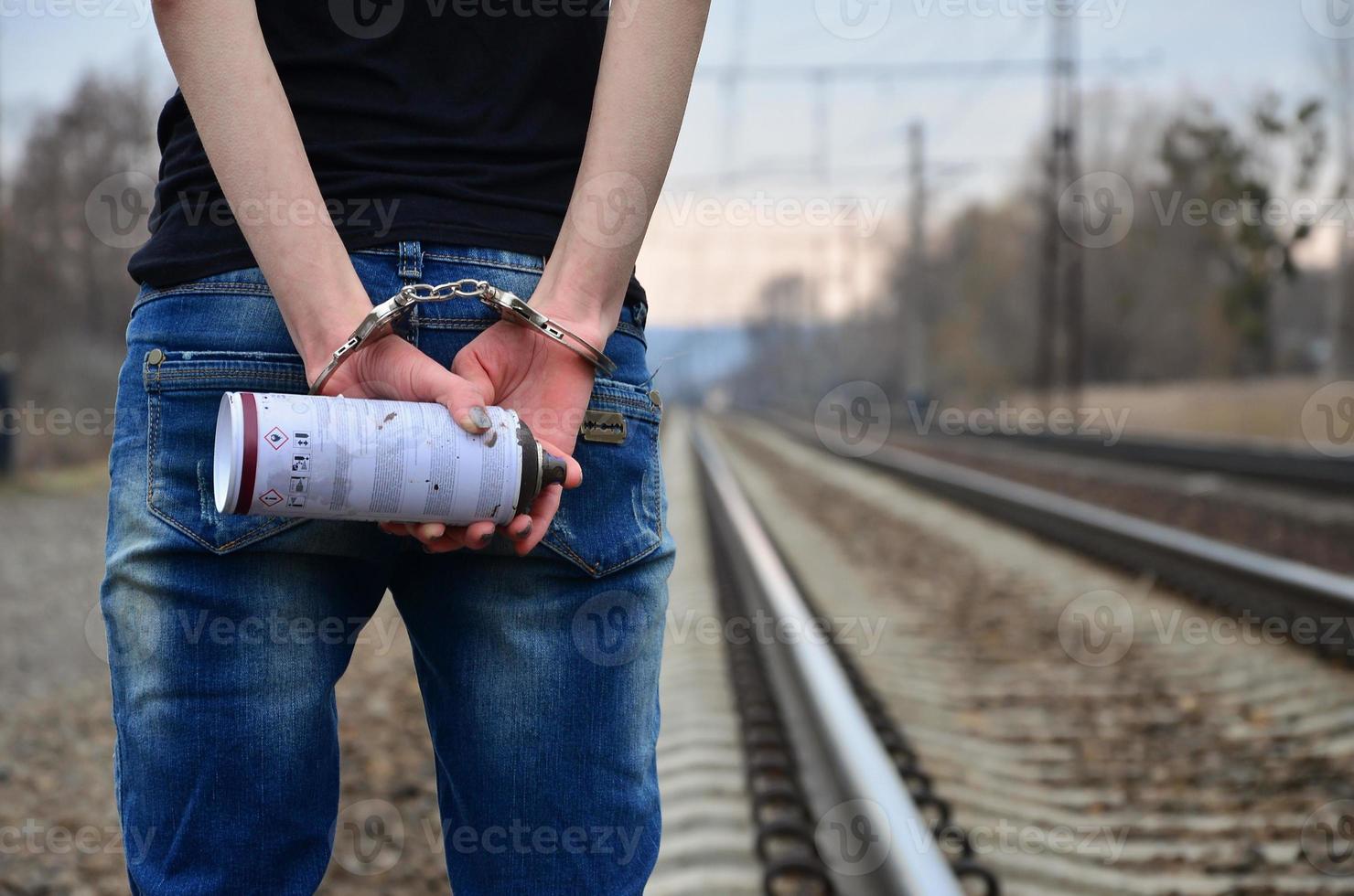Girl in handcuffs with spraycan on the background of a railway t photo