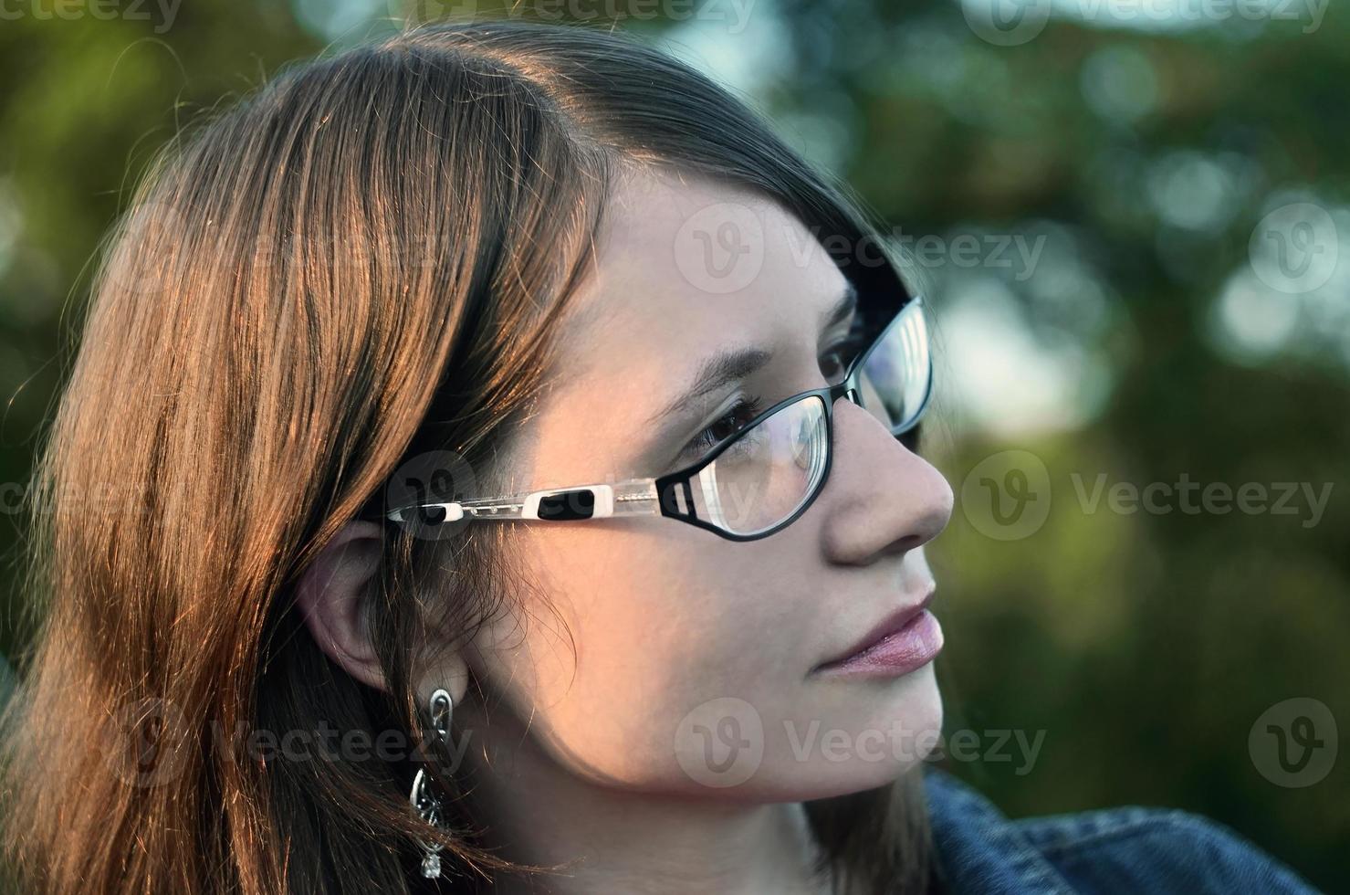 Girl in glasses and jeans jacket is resting on the roof of a hou photo