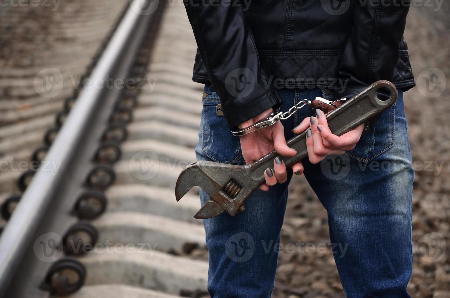 The girl in handcuffs with the adjustable wrench on the railway track background. The concept of crime prevention with the participation of the railway and trains. photo