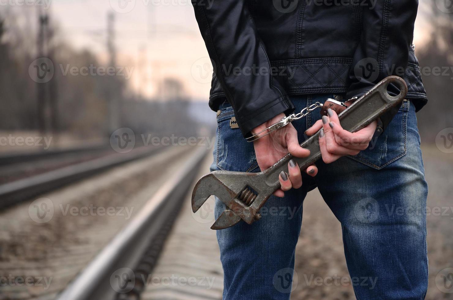 The girl in handcuffs with the adjustable wrench on the railway track background. The concept of crime prevention with the participation of the railway and trains. photo