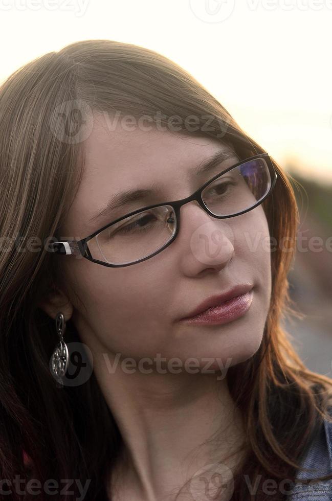 Girl in glasses and jeans jacket is resting on the roof of a hou photo