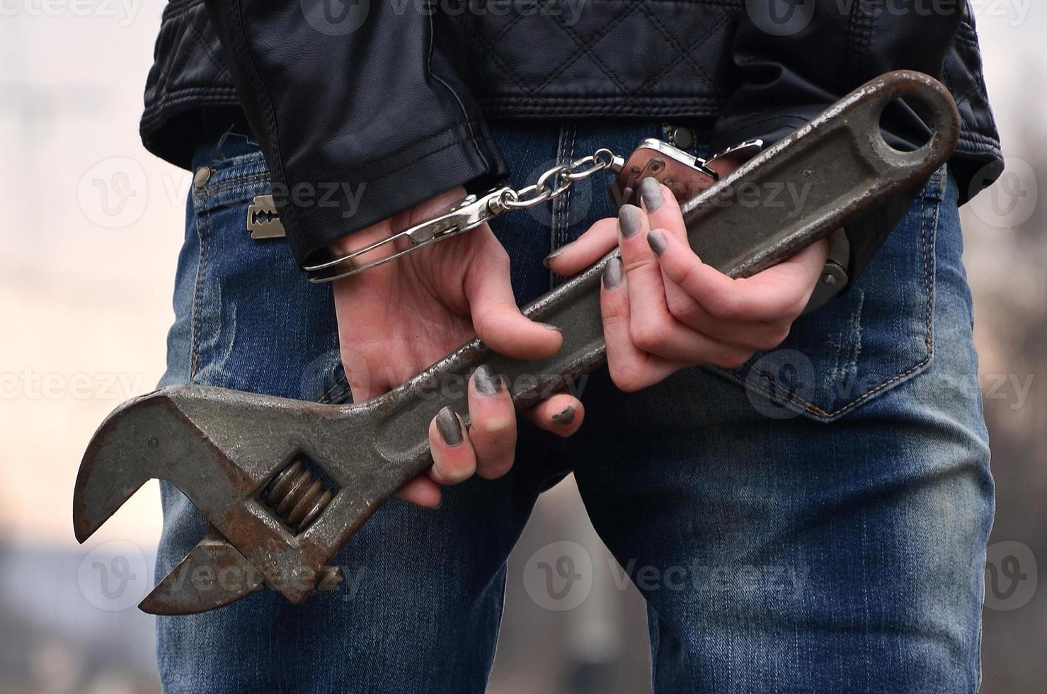The girl in handcuffs with the adjustable wrench on the railway track background. The concept of crime prevention with the participation of the railway and trains. photo