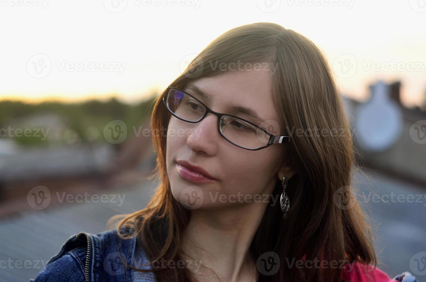 Girl in glasses and jeans jacket is resting on the roof of a hou photo