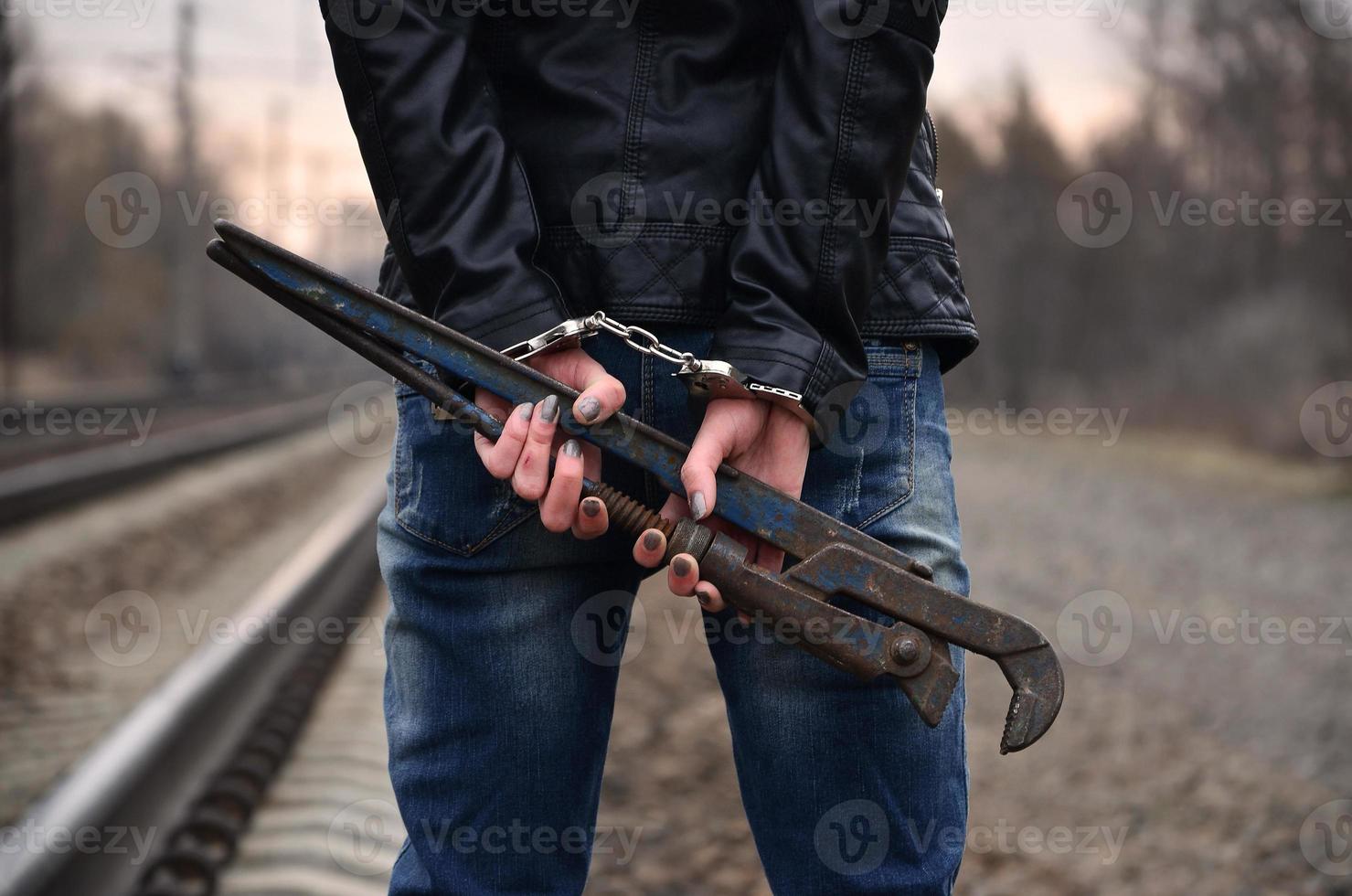 The girl in handcuffs with the pipe wrench on the railway track background. The concept of crime prevention with the participation of the railway and trains. photo