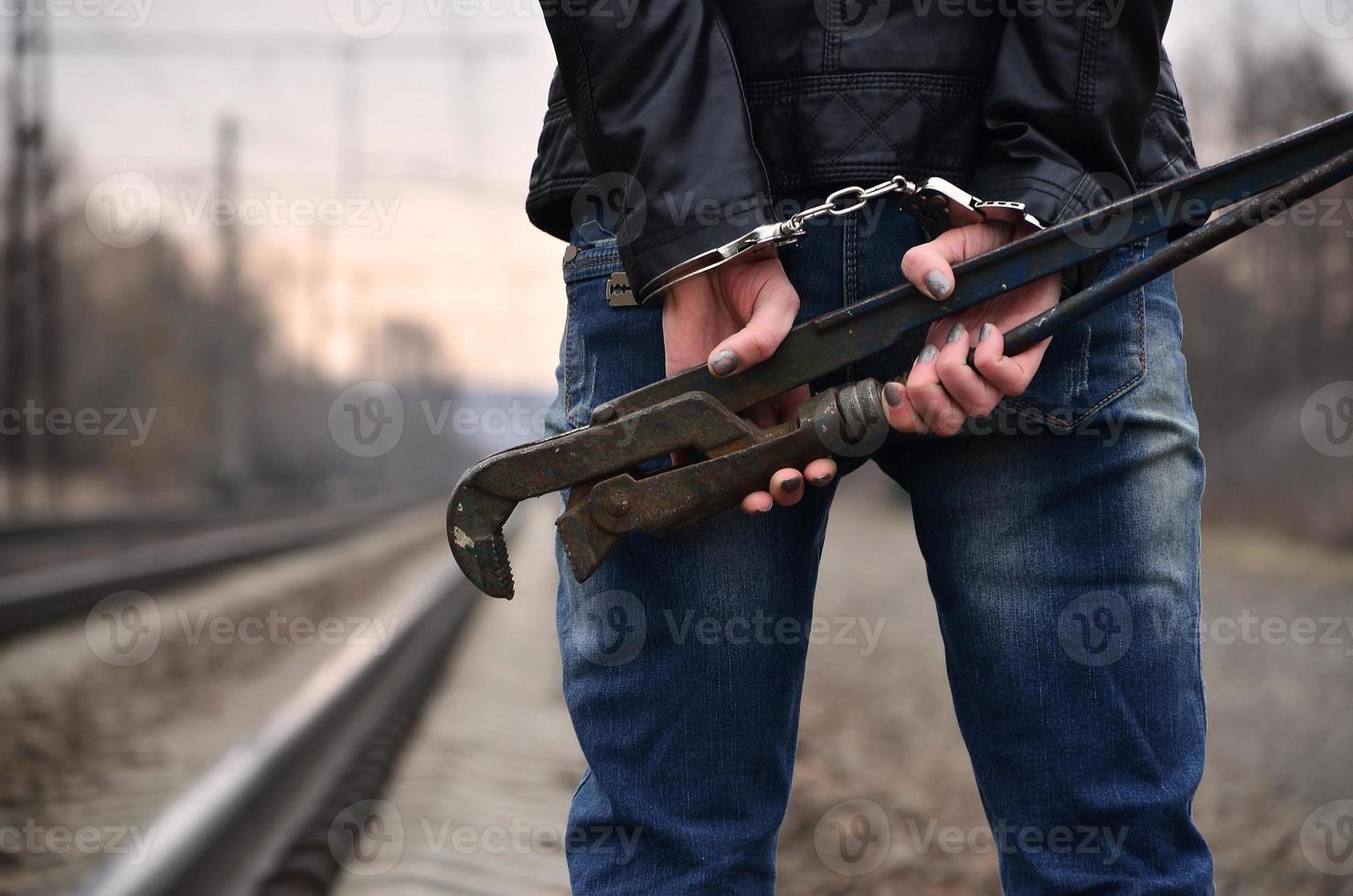 The girl in handcuffs with the pipe wrench on the railway track background. The concept of crime prevention with the participation of the railway and trains. photo