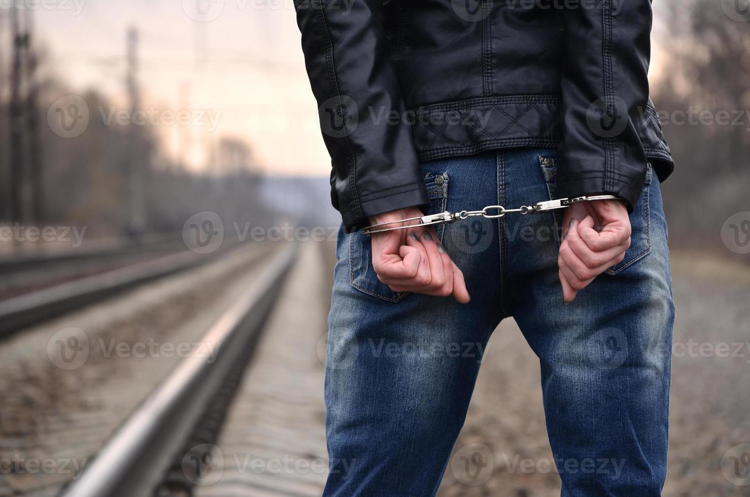 Girl in handcuffs on the background of a railway track. The concept of crime prevention with the participation of the railway and trains. Evening photo of the lower half of the body of a girl