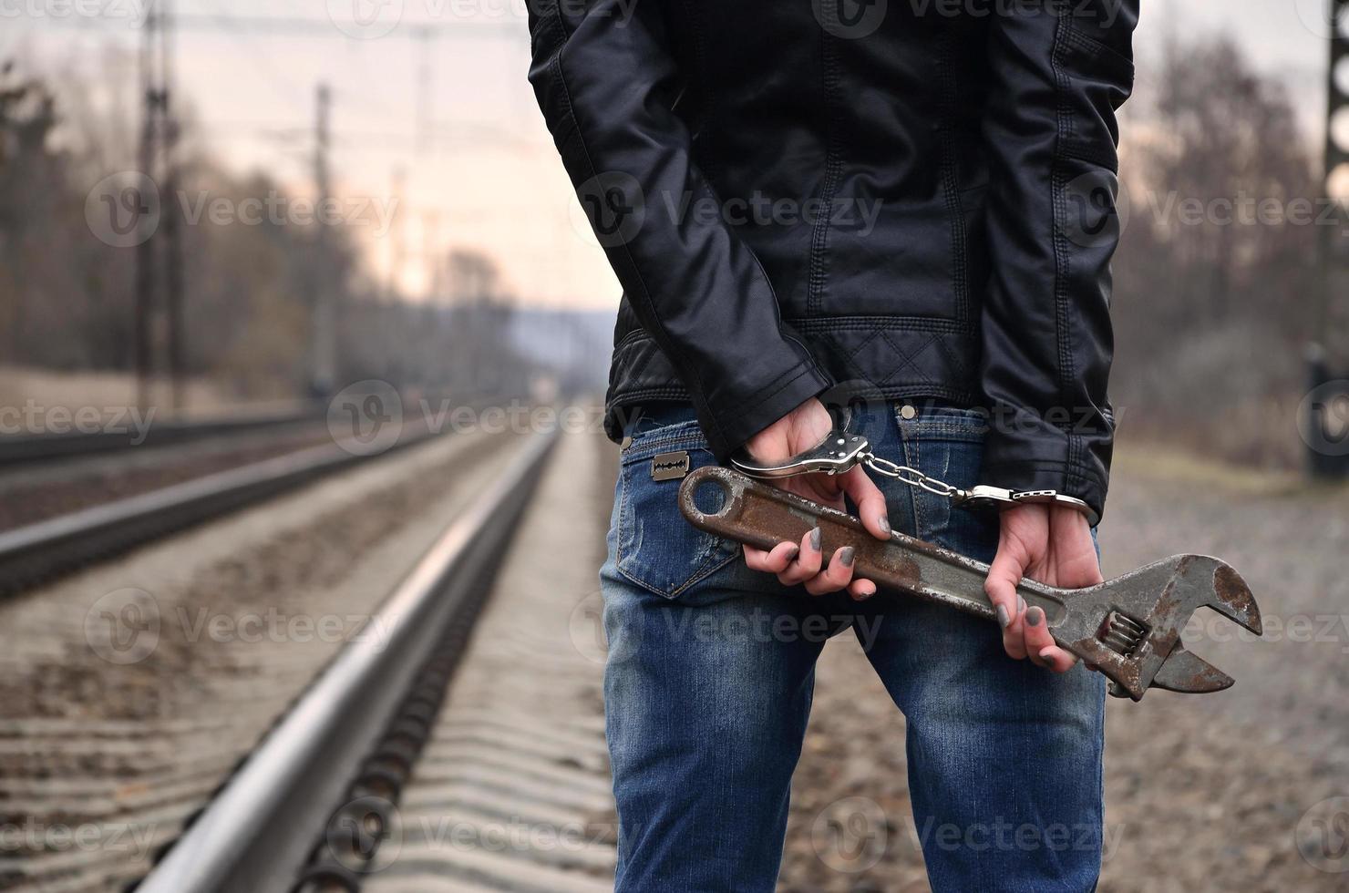 la chica esposada con la llave ajustable en el fondo de la vía férrea. el concepto de prevención del delito con la participación del ferrocarril y los trenes. foto