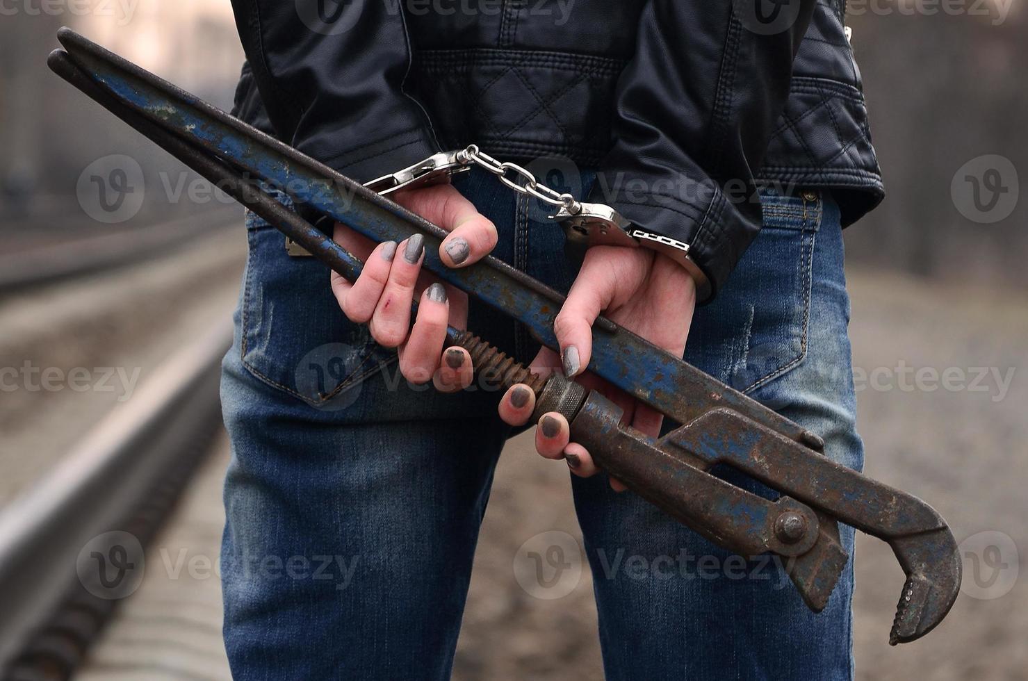 The girl in handcuffs with the pipe wrench on the railway track background. The concept of crime prevention with the participation of the railway and trains. photo
