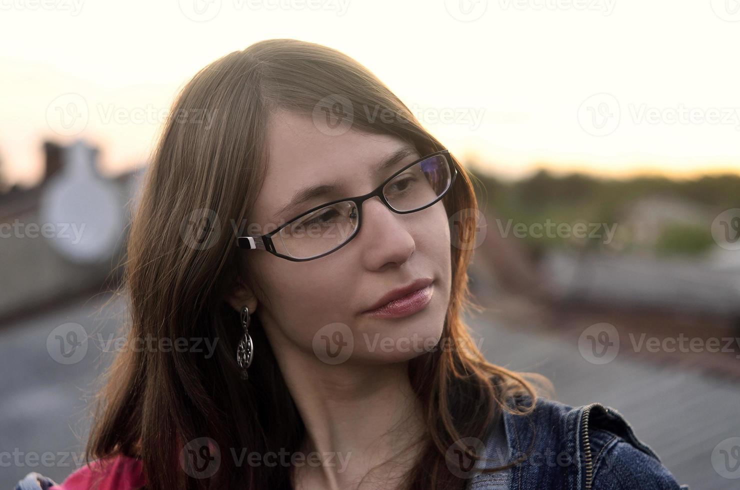 Girl in glasses and jeans jacket is resting on the roof of a hou photo